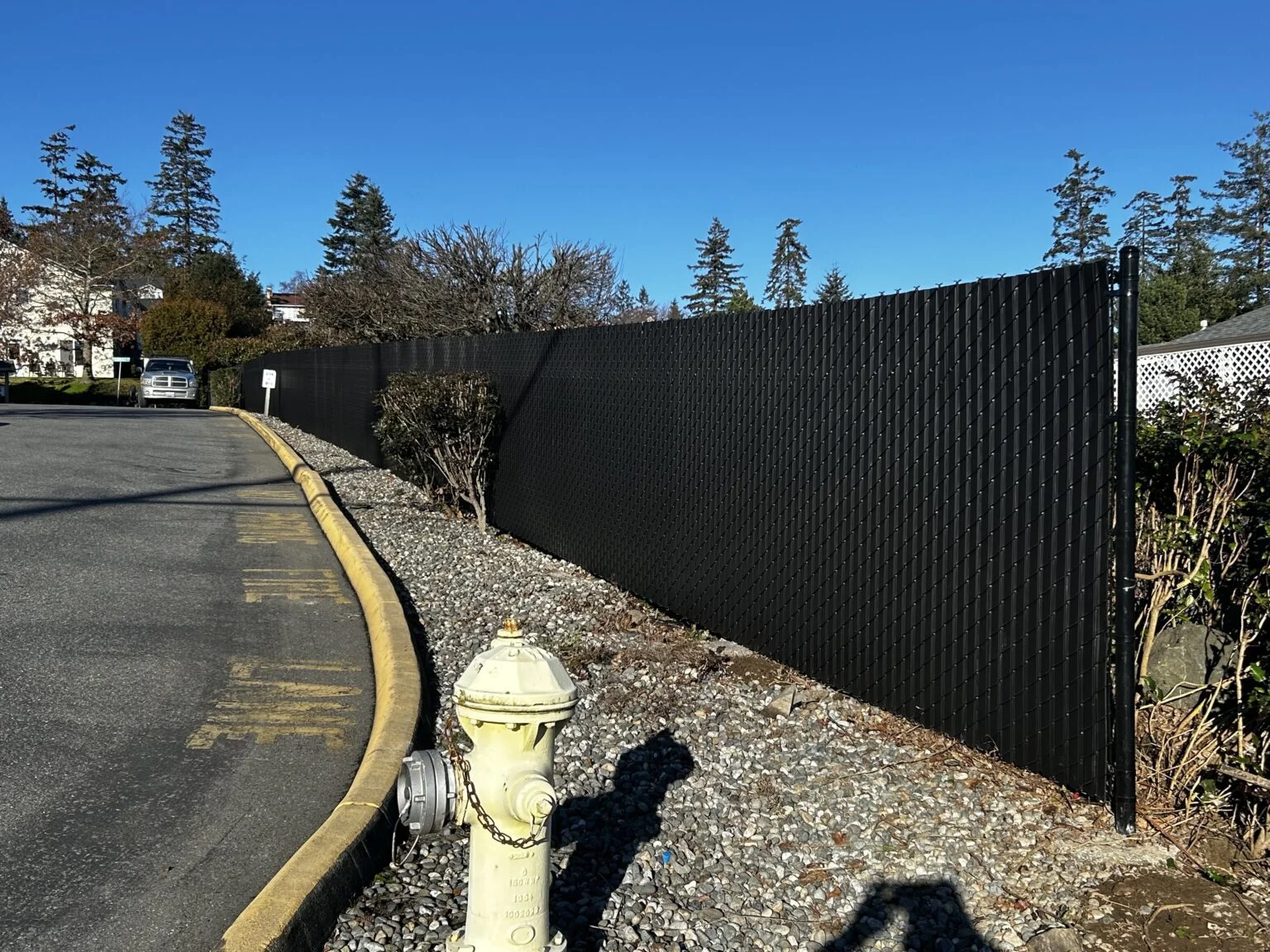Black metal privacy fence installed along residential driveway with gravel base